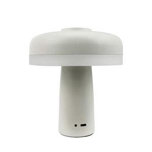 A white mushroom-shaped table lamp stands centrally; it has a cylindrical base, round screen and visible ports (USB‑C and small indicator hole) against a uniform white background.