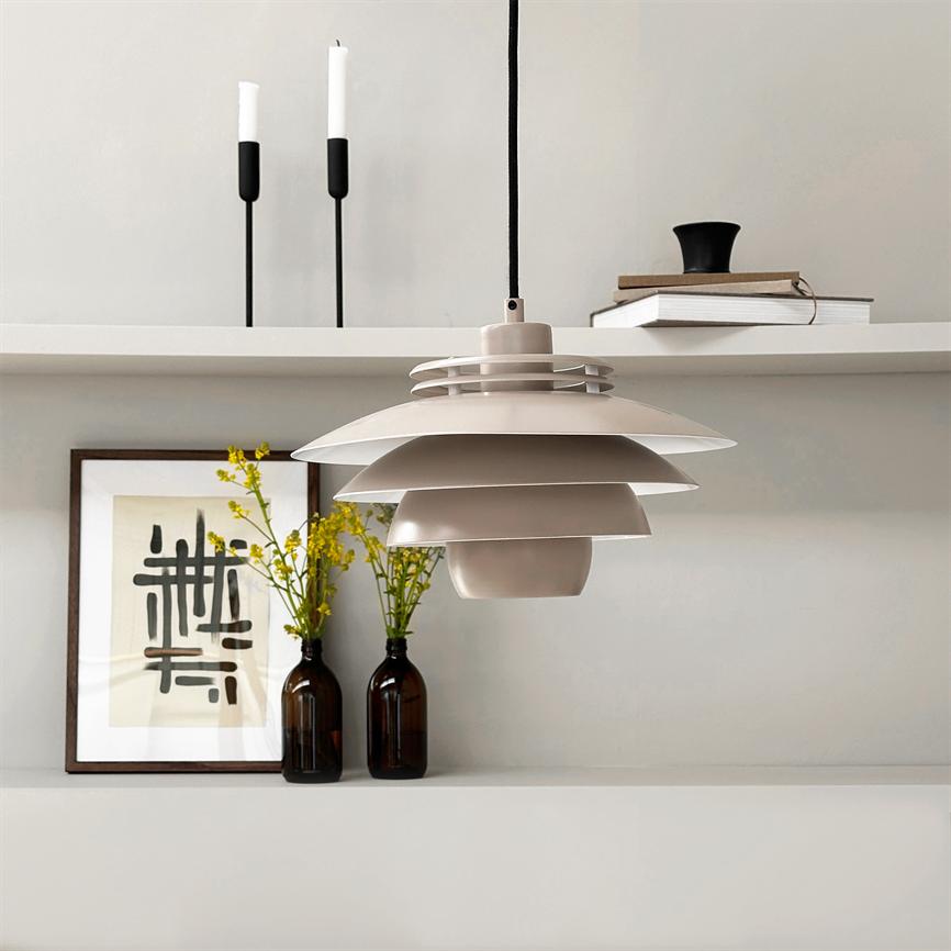 A beige layered pendant lamp hangs above a minimalist shelf with two brown glass bottles with yellow flowers, a framed abstract poster, two black candlesticks and a small bookshelf.
