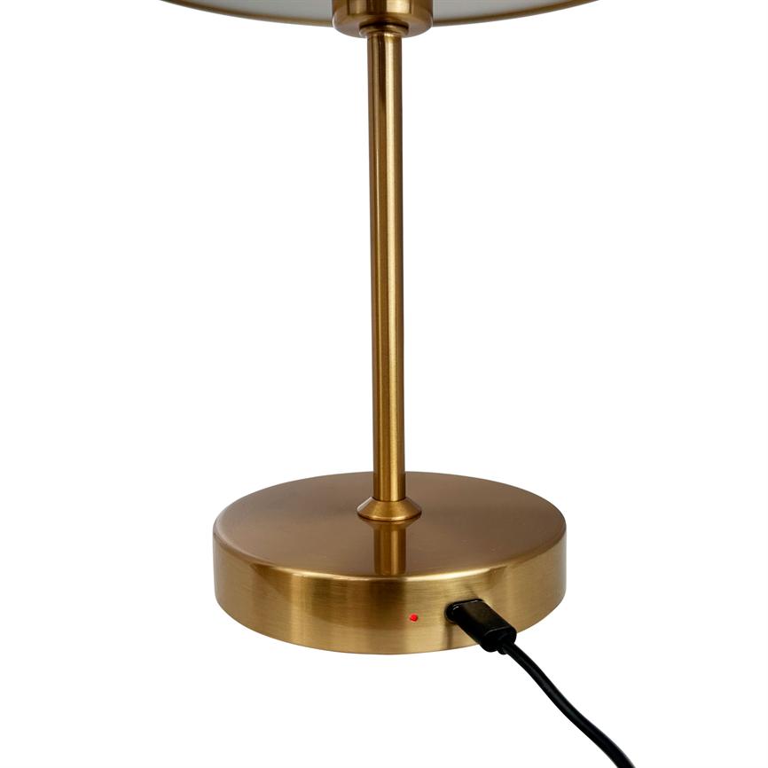 Table lamp base in brushed brass stands vertically; a black USB cable is connected to the base input and a small red LED lights up; neutral white background with no other objects.