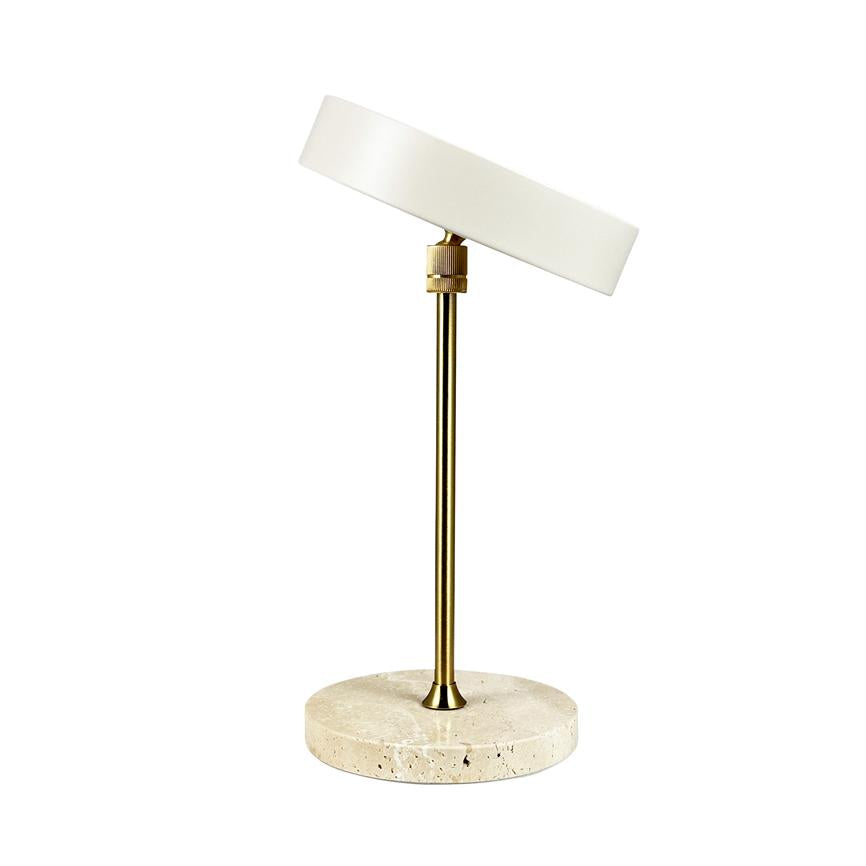 Table lamp stands, its adjustable round white shade is slightly angled on a slender brass rod, mounted on a round light travertine base against a white background.