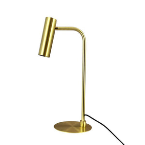 Brass table lamp with cylindrical shade angled downwards; slender curved bar on round base, black cord lying out to the side against pure white background.