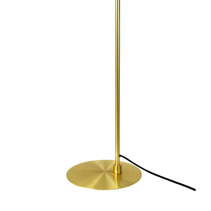 Slender gold colored lamp post stands vertically, fixed in a round, flat brushed brass base; a black power cord runs from the base against a neutral white background.