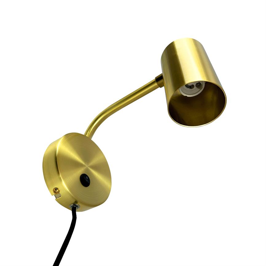 Wall lamp in brushed brass; a curved arm holds an open cylindrical lampshade; the base plate of the lamp has a black on/off button and a black cord hangs down against a white background.