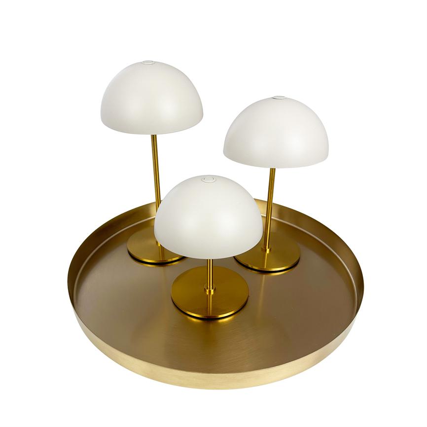 Three small table lamps with white domes and golden stands stand together on a round, matt golden metal dish against a neutral white background.