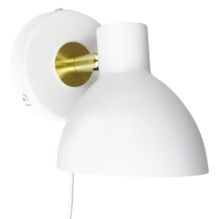 White wall lamp with round shade and brass link, mounted on round wall bracket; the screen tilts downwards, white fabric cord hangs freely against a uniform white background.