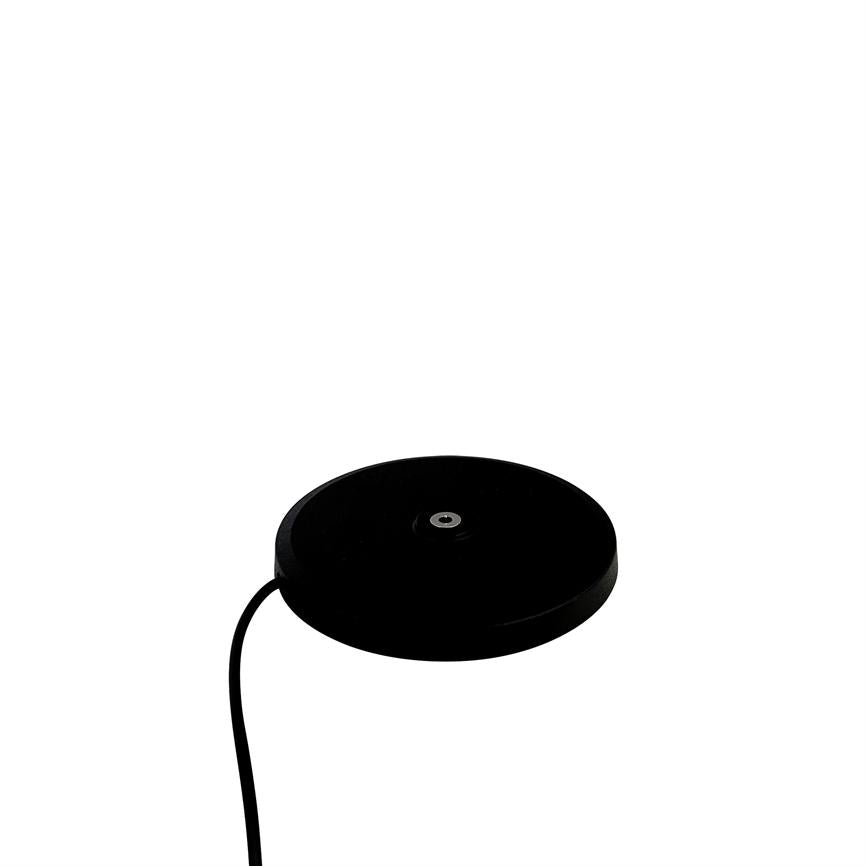 Round, black wireless charger with small metal ring in the middle, connected to a black wire, placed against a uniform white background.
