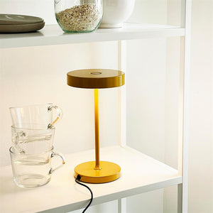 Yellow table lamp is lit on a white shelf; its black cord winds toward the edge; three transparent cups are stacked next to it, and the top shelf holds glass and china containers.