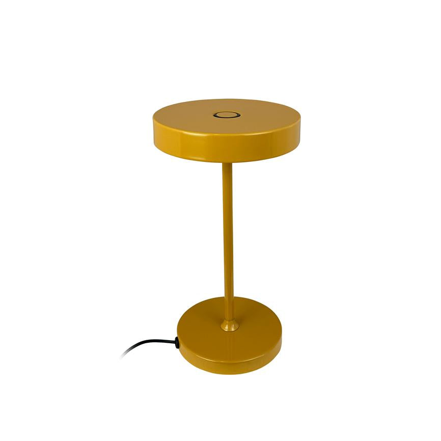 Yellow metal table lamp stands isolated on white background; round shade and foot connected by a slim rod, black power cable lies at the base.