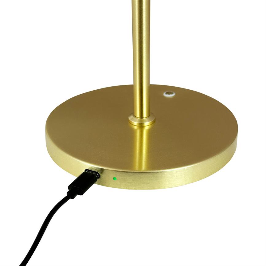 Gold-colored lamp base with vertical rod, where a black USB cable is connected, a small green diode lights up; on a neutral white background.