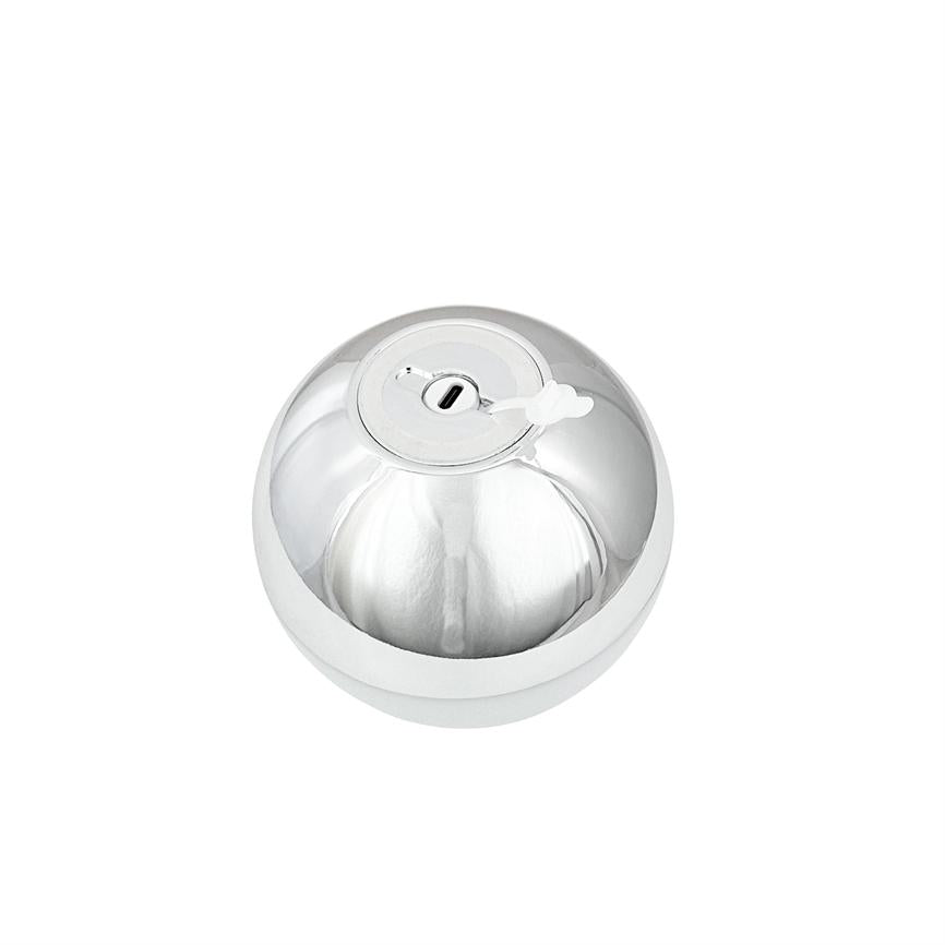 A shiny silver sphere with a round top cap and small white rubber plug covering a rectangular opening; it lies still on a white, uniform background.