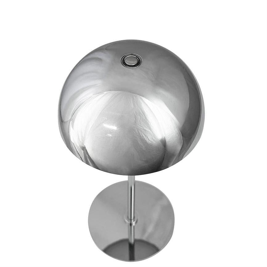 Krom bordlampe med rund kuppel, står på slank stolpe; kuppelen reflekterer hvidt stof og lys mod en neutral hvid baggrund.