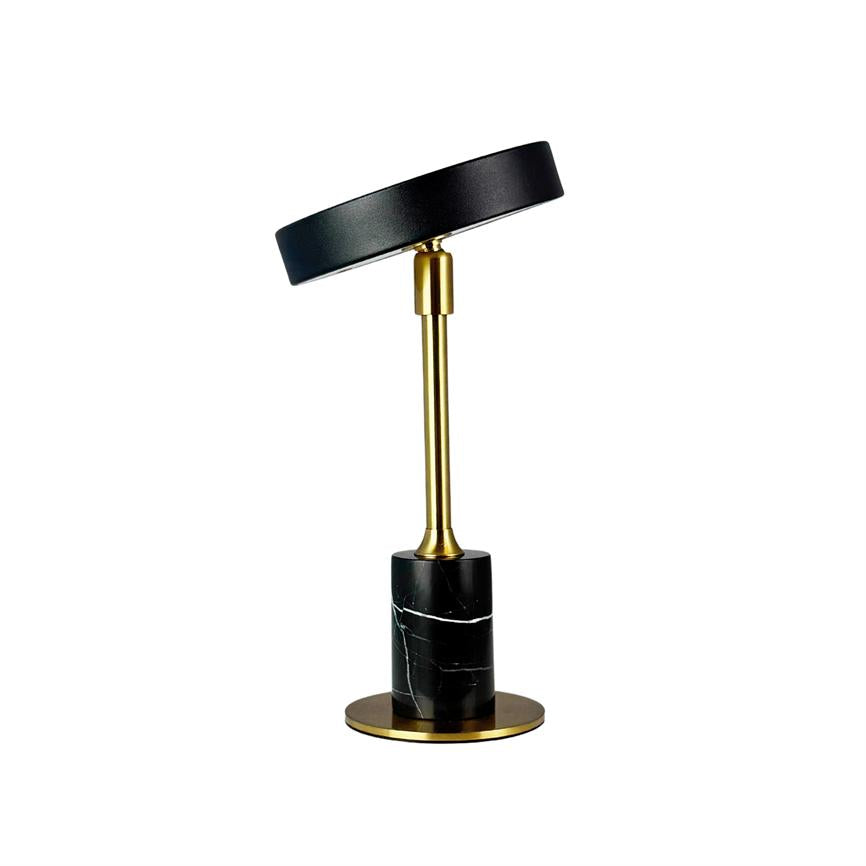 Table lamp with black, slightly tilted shade, gold-coloured rod and cylindrical black marble base with white veins, placed on a round gold-coloured base against a white background.