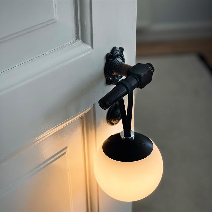 A globe-shaped lamp hangs from a strap from an ornamented doorknob, casting warm, soft light on a white paneled door in a dim, carpeted hallway.