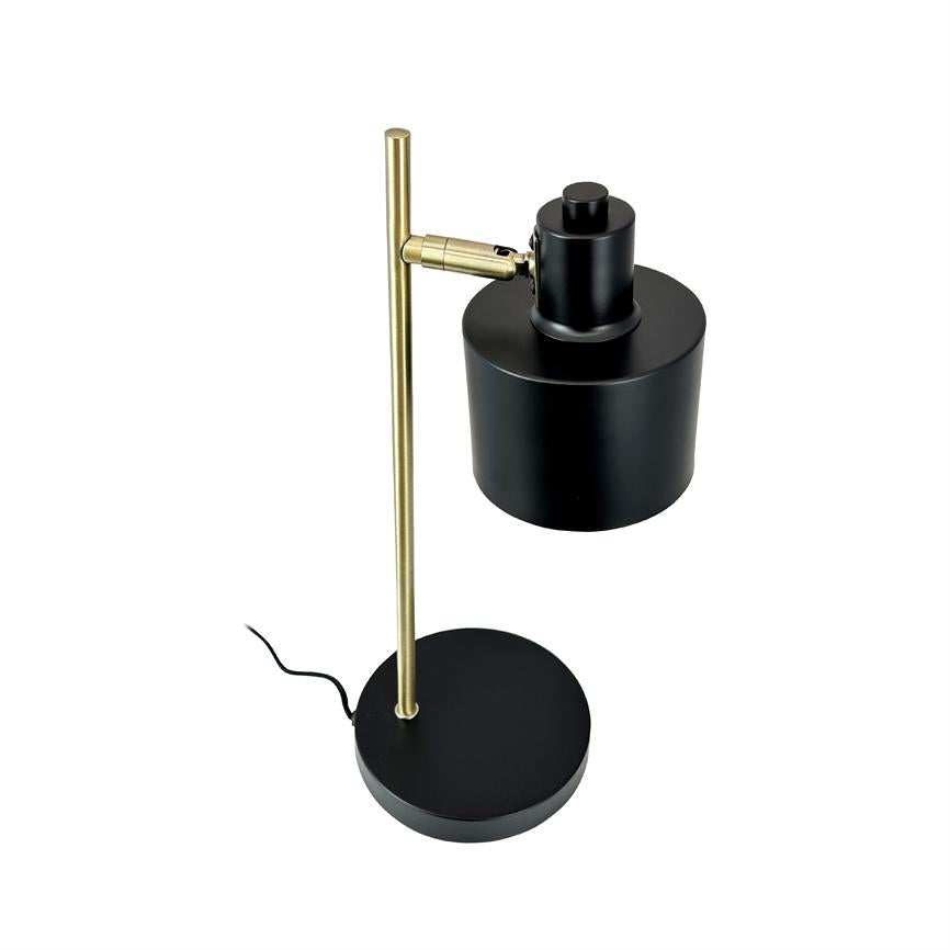 Black table lamp stands on round black base, with a vertical brass rod, adjustable black cylindrical shade mounted on short arm and visible black cord; white background.