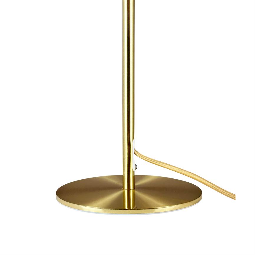 Gold-coloured lampstand stands upright on flat round base, cable passes through small bracket and exits to right; white background.