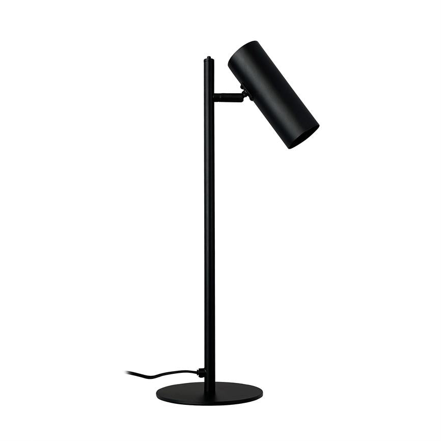 Black table lamp with cylindrical shade, angled downwards; stands on slender vertical pole and round foot, with visible power cord, placed in front of a white, neutral background.