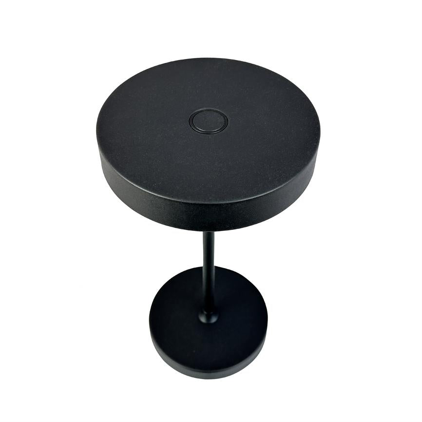 Black, round table lamp with flat lamp head and small central push button, mounted on a thin rod above a round foot; placed against a uniform white background.