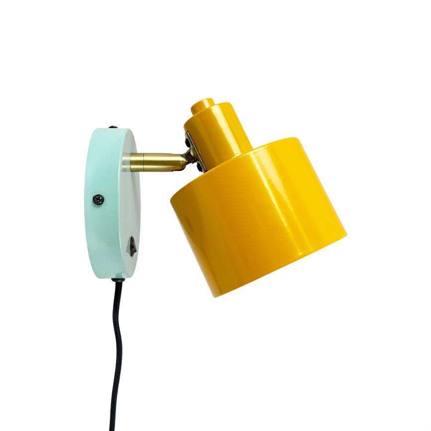 Yellow metal wall lamp angles obliquely downwards, mounted on a mint green round wall plate via a brass connection; black cord hangs down against a uniform white background.
