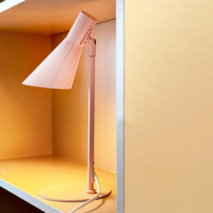 Table lamp (pink) is lit on a shelf in a built-in niche, casting warm yellow light against matte pale yellow walls, with white cord twisted at the base.