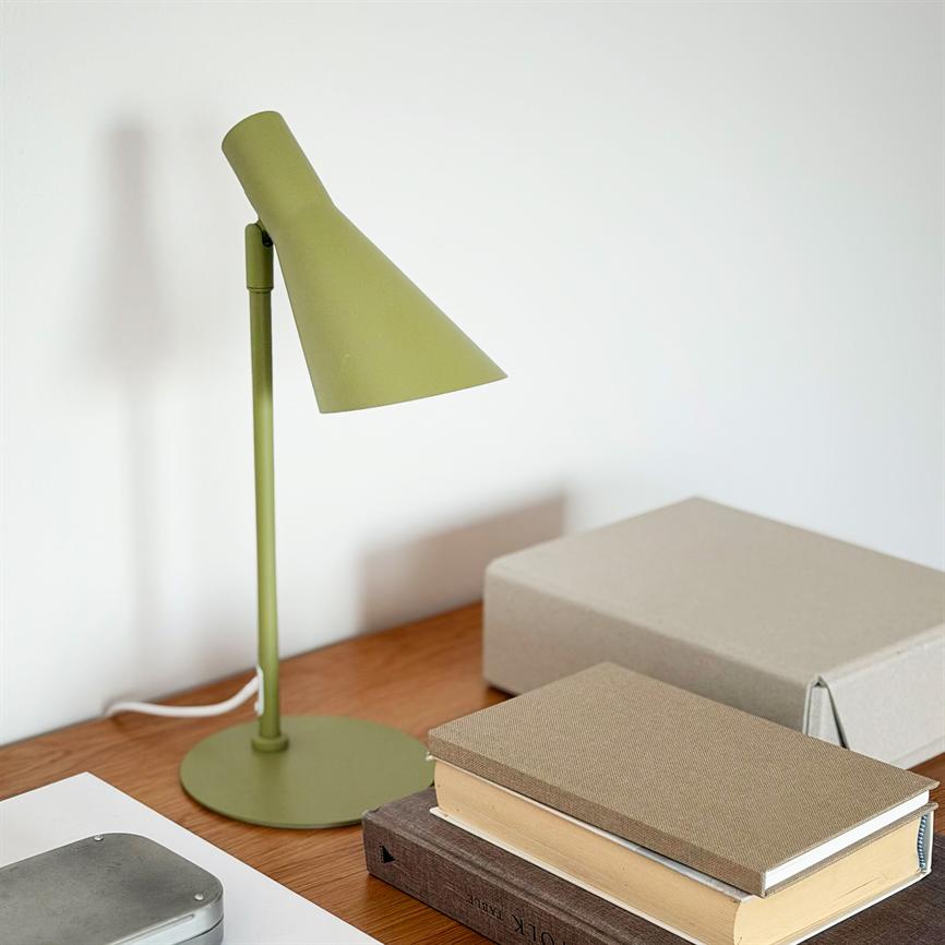 Green desk lamp stands next to a stack of books and a gray box; the lamp casts a soft shadow against a white wall on a wooden table.