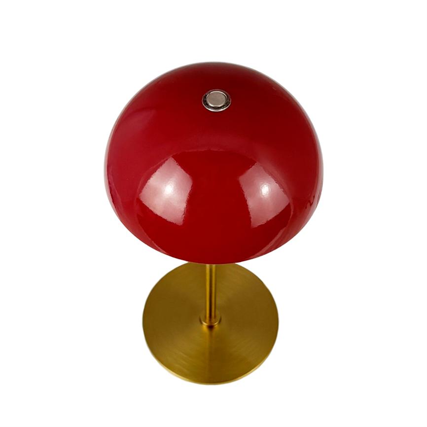 Red, glossy lamp dome mounted on a slender brass rod and round brass base, stands on a white background; the screen's surface reflects light and has a small metal button at the top.