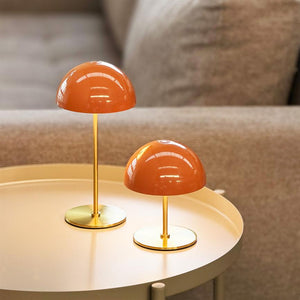 Two small orange table lamps stand on a round table, reflect light and are placed in front of a beige sofa in a quiet, cozy living room.