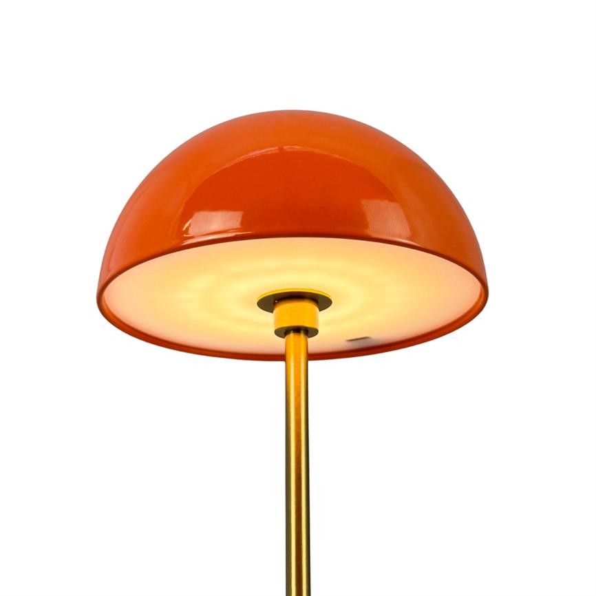 An orange, dome-shaped lampshade emits warm light downwards from a slender, gold-colored rod against a clean, white background.