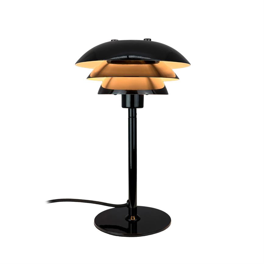 Bordlampe med tre lag skærme lyser med varmt skær; den står på en slank sort stamme med rund fod; omgivelserne er en ren, hvid baggrund.