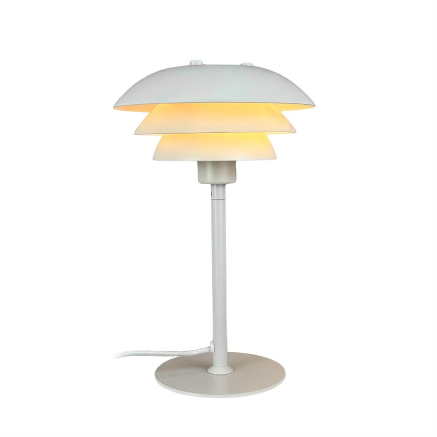 En hvid, trelags bordlampe udsender varm, diffus glød; står på slank søjle med rund fod og synlig ledning mod en neutral, hvid baggrund.